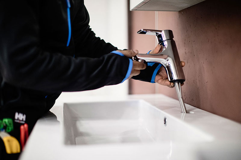 En VB-rørlegger installerer nytt batteri på en baderomsvask